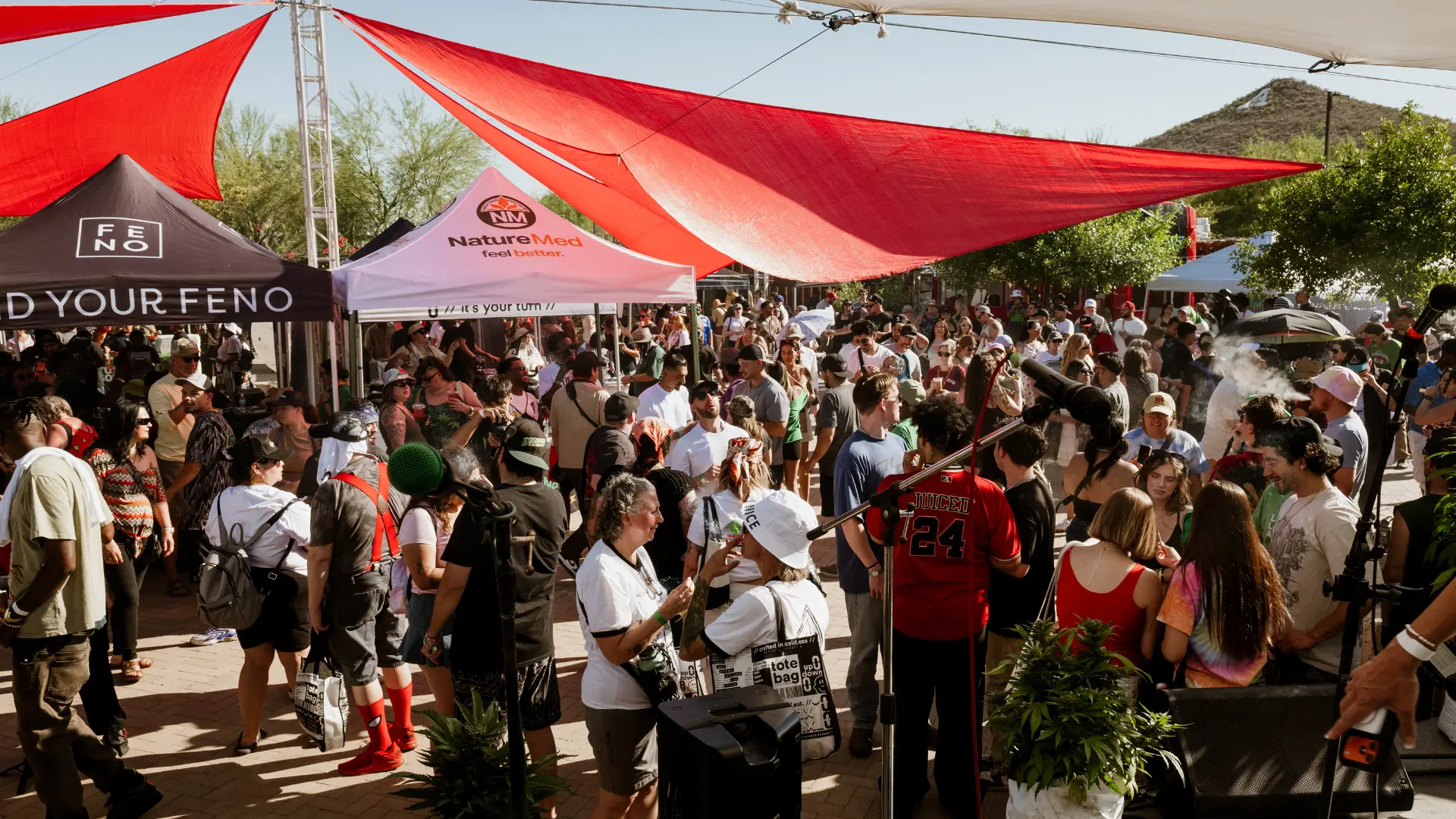 A large daytime crowd at the Tucson 420 Festival gathered under red shade sails.