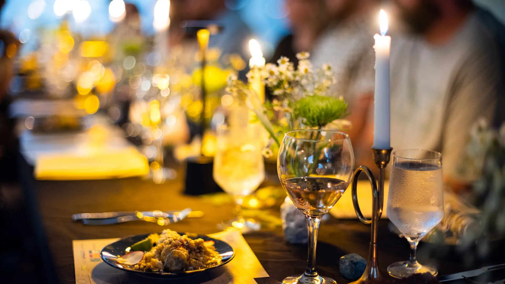 A candlelit dinner table set with wine glasses and fresh flowers.